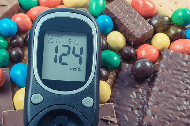 glucose meter for checking sugar level and heap of sweets containing a lot of sugar
